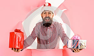 Bearded man in Santa hat and checkered shirt with presents gifts boxes looking through paper hole.