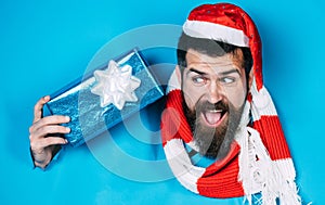 Bearded man in santa hat with present gift box looking through paper hole. Christmas sale. Discount.