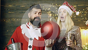 Bearded man in a santa`s costume and a blond girl with astonished faces holding in their hands of a burning bomb. New