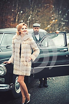 Bearded man and sexy woman in fur coat. Escort of girl by security. Retro collection car and auto repair by mechanic