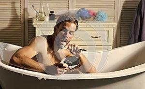 Bearded man shave beard with razor in bathtub in bathroom