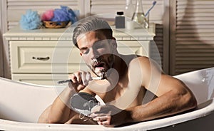 Bearded man shave beard with razor in bathtub in bathroom. Bearded man with shaving soap on beard look in mirror.