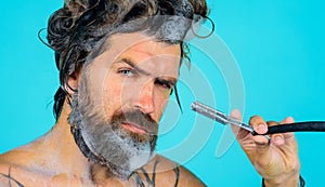 Bearded man shaving beard with straight razor in shower. Beard Care. Beauty, hygiene, grooming and people concept.