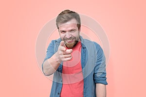 A bearded man shows his finger in front of him and maliciously smiles ridiculing someone. Isolated on coral background photo
