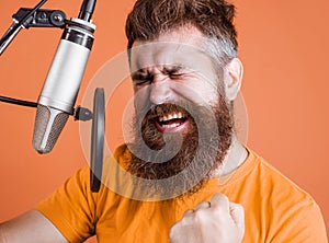 Bearded man sings in condenser microphone at recording studio. Emotional Male professional vocalist.