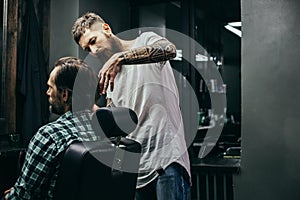 Bearded man sitting in the armchair and calm barber cutting his hair