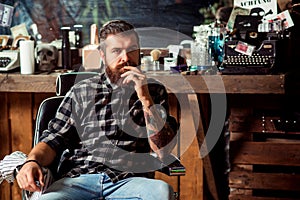 Bearded man sitting in chair at barbershop. Handsome barber man. Barber shop. Bearded hipster with tattooe on his arms