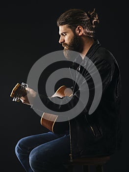 Bearded man sitting playing an acoustic guitar