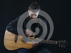 Bearded man sitting playing an acoustic guitar