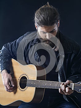 Bearded man sitting playing an acoustic guitar