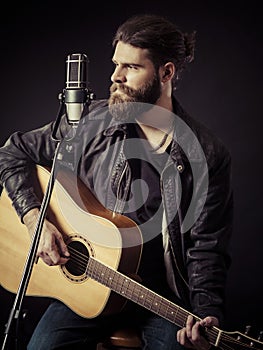 Bearded man sitting playing an acoustic guitar