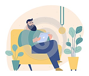 Bearded man sitting on yellow armchair with tablet. Casual male in home interior using digital device. Freelancer works