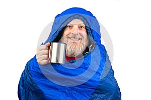 bearded man in a sleeping bag with a cup of coffee on a white background. equipment for recreation in tourism and travel