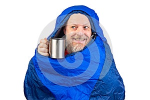 bearded man in a sleeping bag with a cup of coffee on a white background. equipment for recreation in tourism and travel