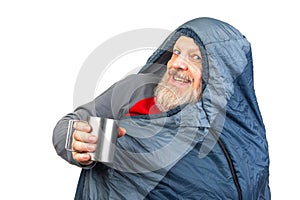 bearded man in a sleeping bag with a cup of coffee on a white background. equipment for recreation in tourism and travel