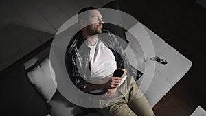 Bearded man sleeping on the couch in a room at home, holding mobile phone