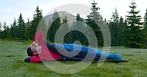 Bearded man sleeping in a sleeping bag on a beautiful meadow in the mountains