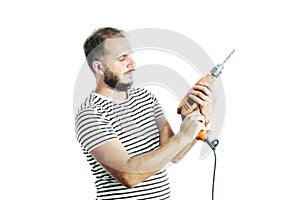 A bearded man in a striped T-shirt, holds an electric drill in his hands with a questioning look