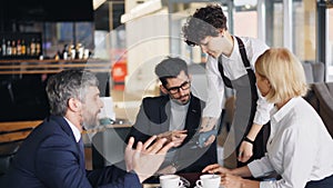 Bearded man in suit making online payment in cafe then talking to coworkers