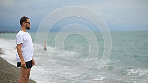 Bearded man in sunglasses on the beach looking at the sea waves