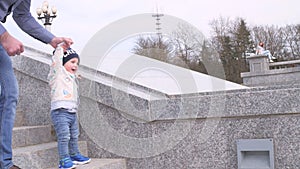 Bearded man in sunglasses holding his little son by the hand helps the happy baby boy to go down the granite ladder step