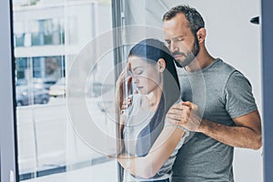 bearded man supporting sad stressed woman with closed eyes standing