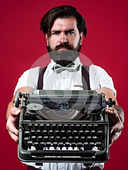 bearded man in suspenders with retro typewriter. brutal guy in bow tie. elegant male typist. handsome hipster use