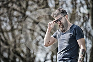 Bearded man takes off sunglasses on sunny day. Masculinity concept. Man with long beard looks stylish and confident. Man