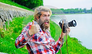 Bearded man taking photo with camera on river. Hobby and travel. Smiling man with professional digital camera.