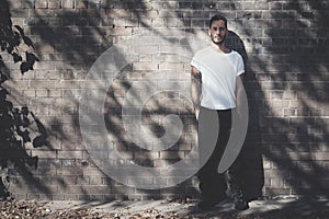 Bearded man with tattoo wearing blank white tshirt and black jeans. Bricks wall background. Horizontal mockup