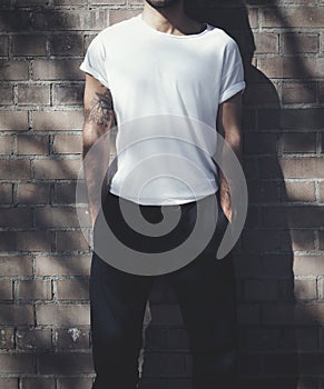 Bearded man with tattoo wearing blank white tshirt and black jeans. Bricks wall background. Vertical mockup, soft