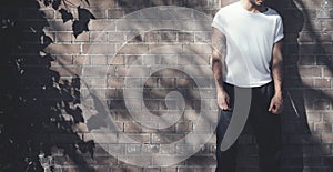Bearded man with tattoo wearing blank white tshirt and black jeans. Bricks wall background. Wide mockup