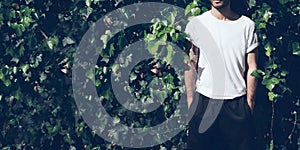 Bearded man with tattoo wearing blank white tshirt and black sunglasses.Green garden wall background. Wide closeup