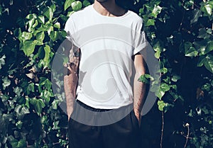 Bearded man with tattoo wearing blank white tshirt.Green garden wall background. Horizontal mockup