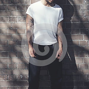 Bearded man with tattoo wearing empty white tshirt and black jeans. Bricks wall background. Vertical mockup