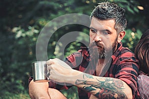 Bearded man with tea or coffee cup in forest. Tourist in plaid shirt hold mug. Hipster with long beard relax on natural