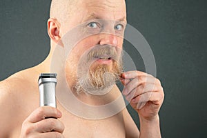 Bearded man with trimmer to adjust beard in hand. grooming and fashionable style barbershop. Beard length correction