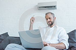 bearded man turning on air conditioner with remote control while