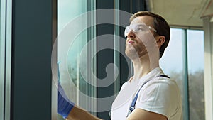 Bearded man in uniform and protective glasses washing office windows