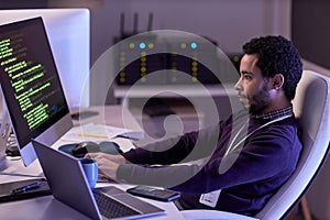 Bearded man using computers and writing code in neon light