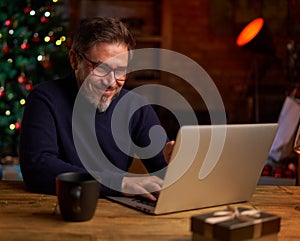 Bearded man using laptop computer at home. Portrait of middle age, mid adult man in 50s shopping online for Christmas, browsing