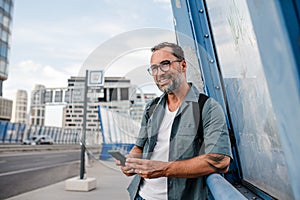 Bearded man using phone while waiting for bus.