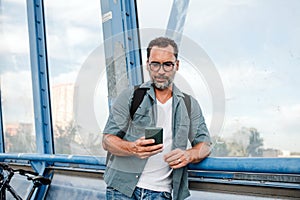 Bearded man using phone while waiting for bus.