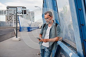 Bearded man using phone while waiting for bus.