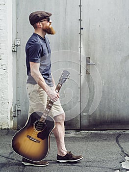 Bearded man walking with acoustic guitar