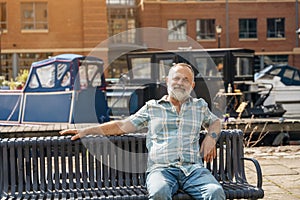 bearded man walking on the quays, pier, sitting on bench, looking at yacht, sailboat, boat. Lifestyle concept