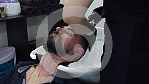 Bearded man washing hair in barber salon. Hairdresser wash male head with water in barbershop salon. Washing hair young