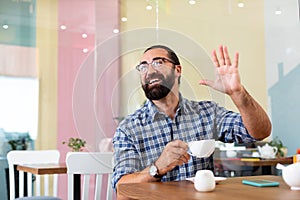 Bearded man waving his hand while seeing old friend in cafe