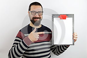 Bearded man wearing eyeglasses wearing casual clothes holding a clipboard with a blank paper pointing with his finger to the side