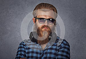 Bearded man wearing sunglasses and headphones. Studio shot on grey background